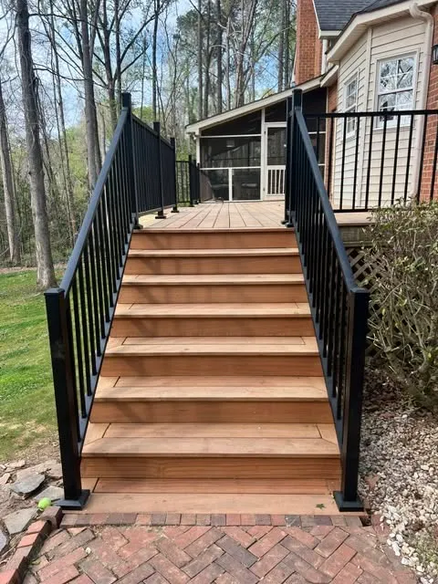Wooden decking steps with black railings leading to a house.